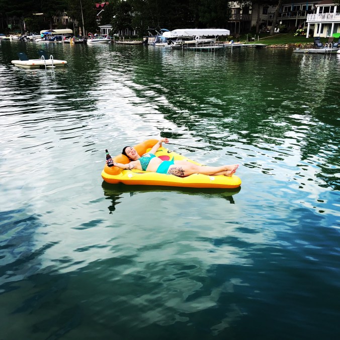 woman floating on pizza-shaped floatie on a lake