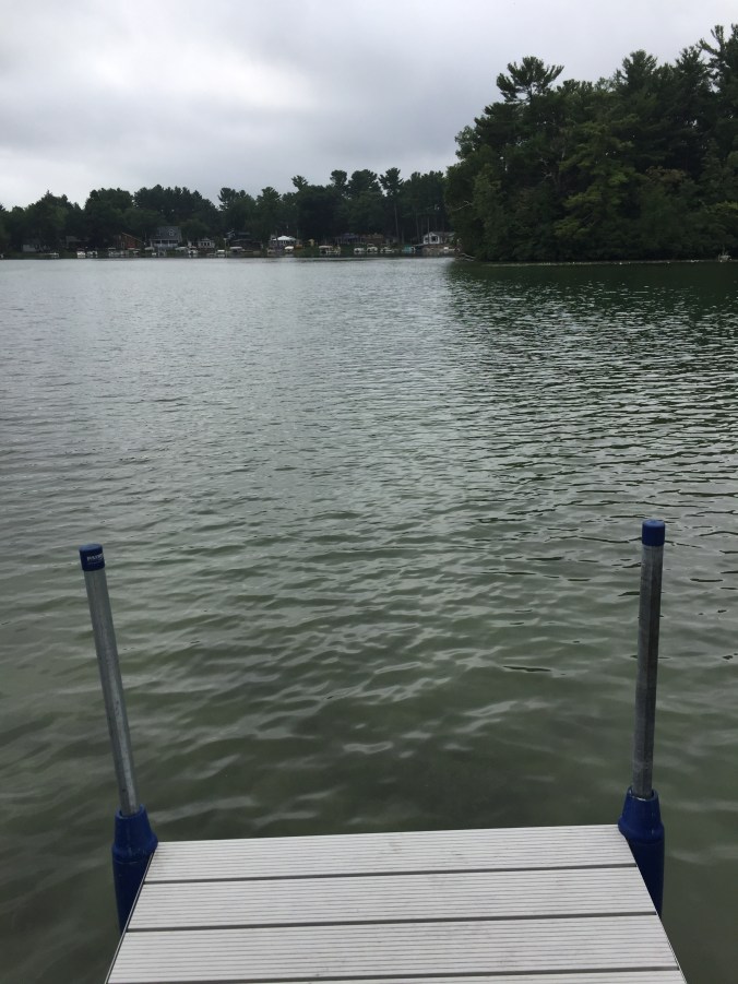 end of a dock facing a lake and a wooded island