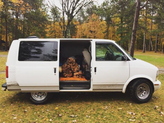 a white chevy astrovan with its sliding door open to reveal a large stack of firewood inside
