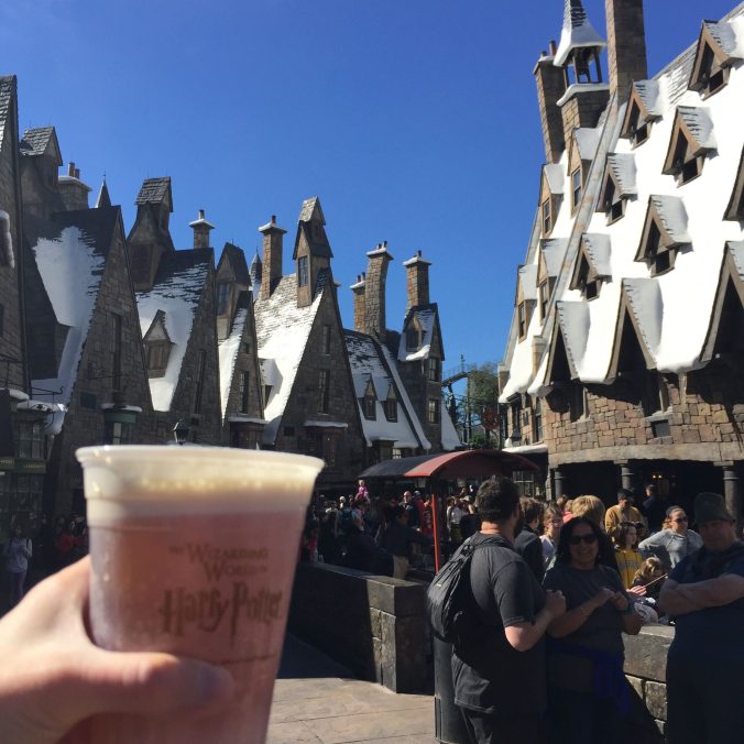 a cup of butterbeer in front of the rooftops of Hogsmeade